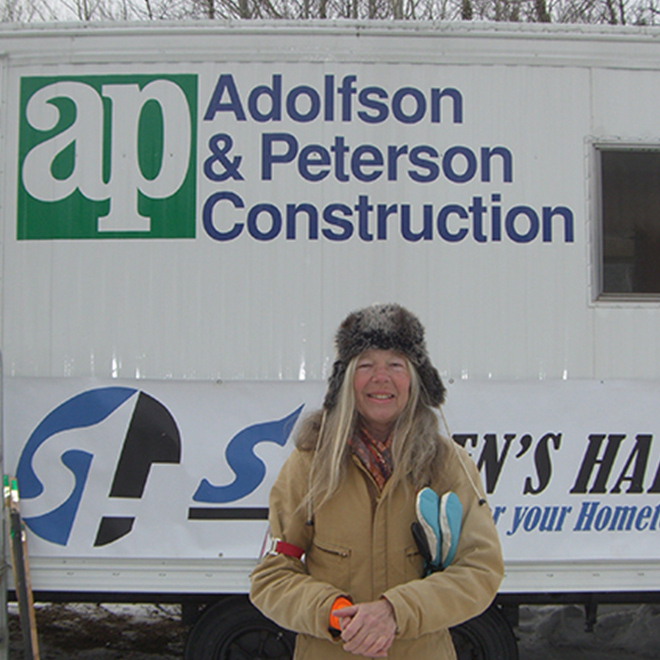 Woman in hat and jacket standing in front of AP Construction sign